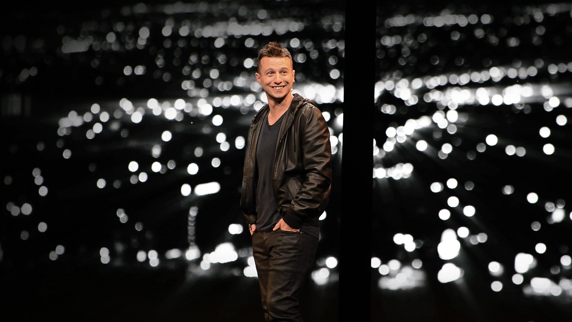 a man wearing a leather jacket on stage and smiling at the audience