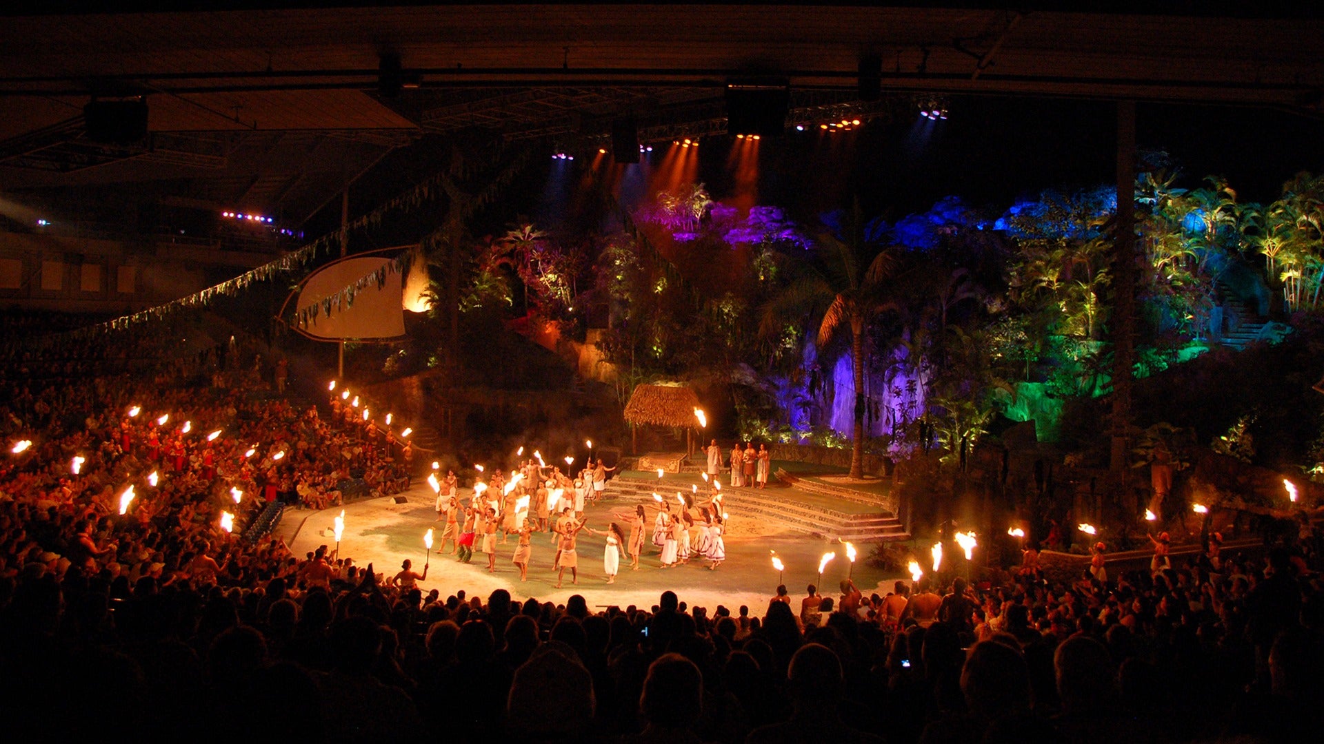 a group of luau dancers and performers on stage with people holding torches
