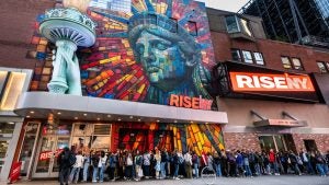 a colorful building with a line of people waiting outside, mural of statue of liberty outside
