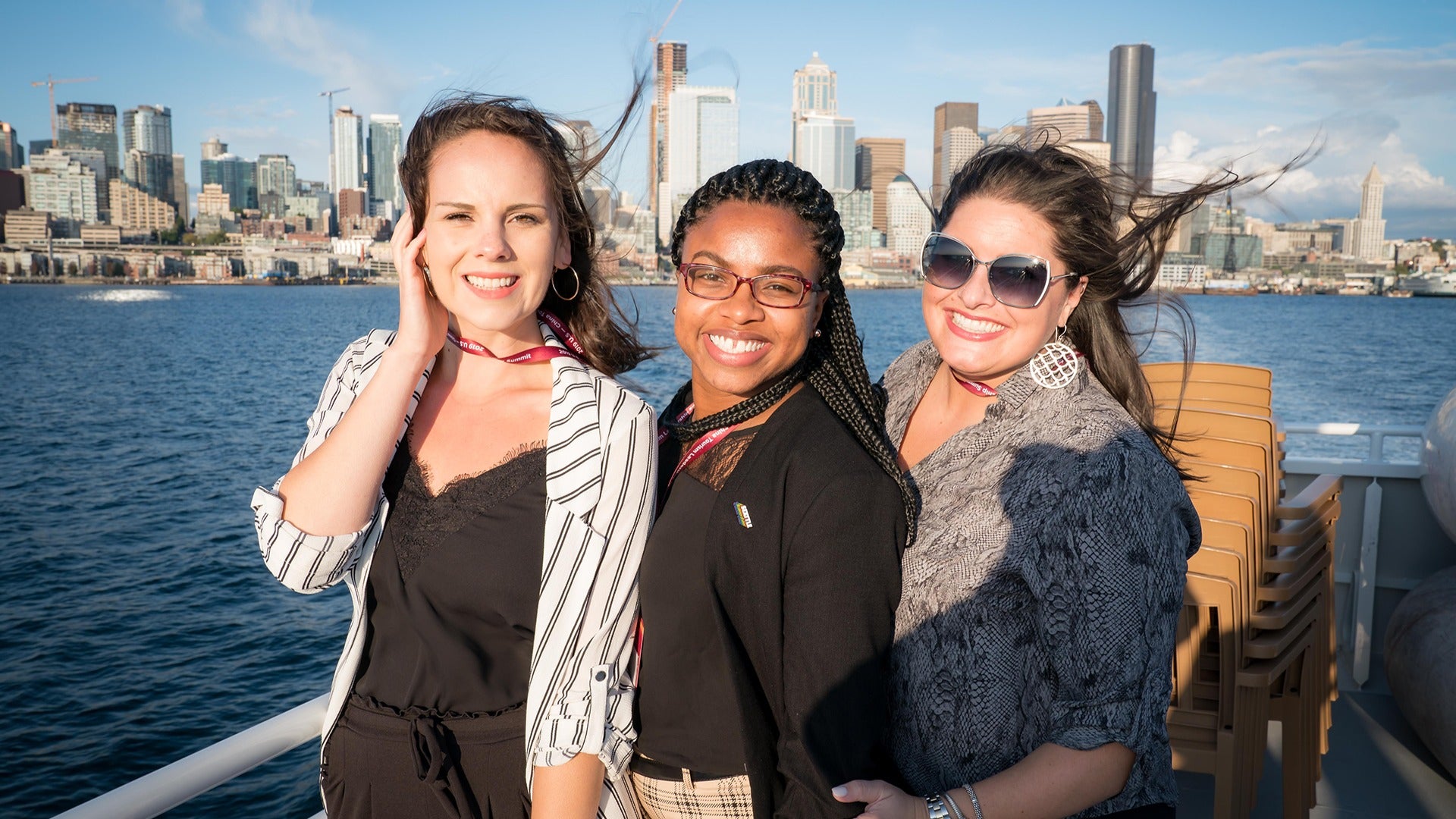 three friends on a cruise smiling with a view of seattle skyline at the back