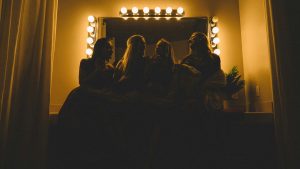 four girls sitting on a makeup vanity with big lights