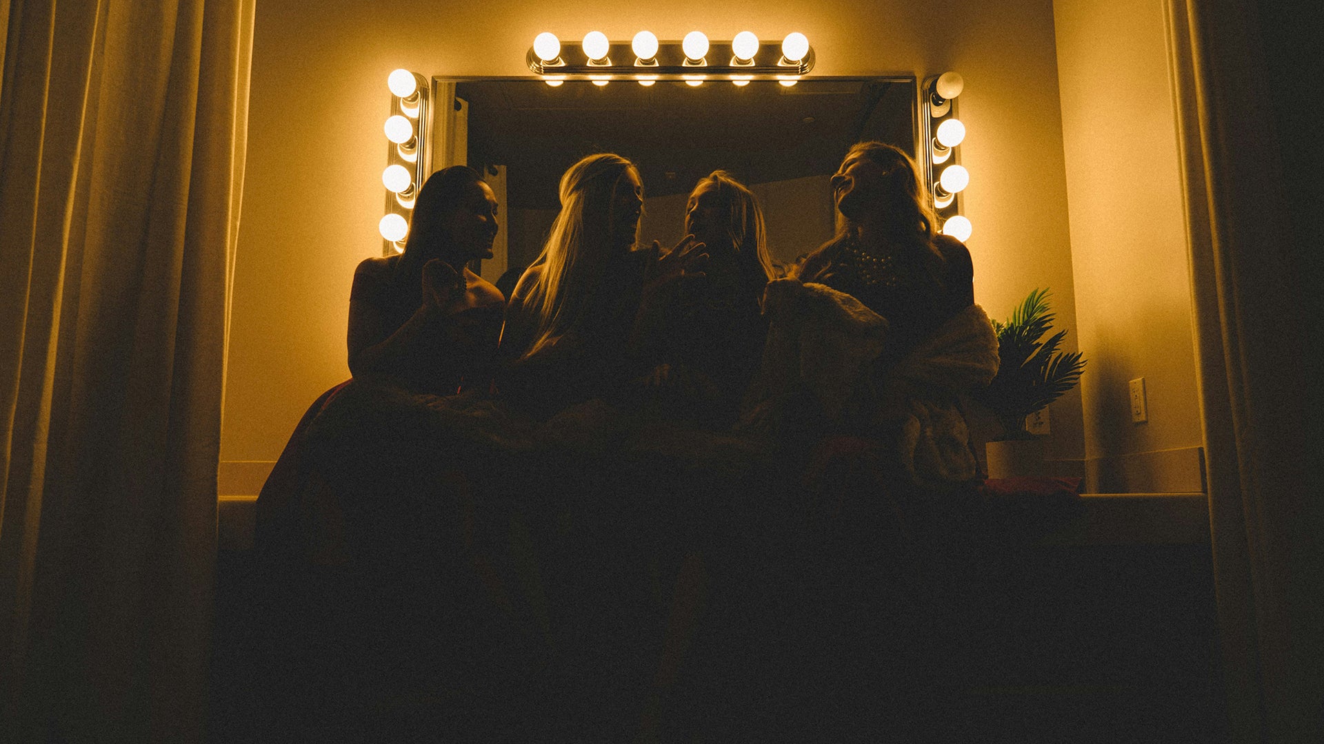four girls sitting on a makeup vanity with big lights