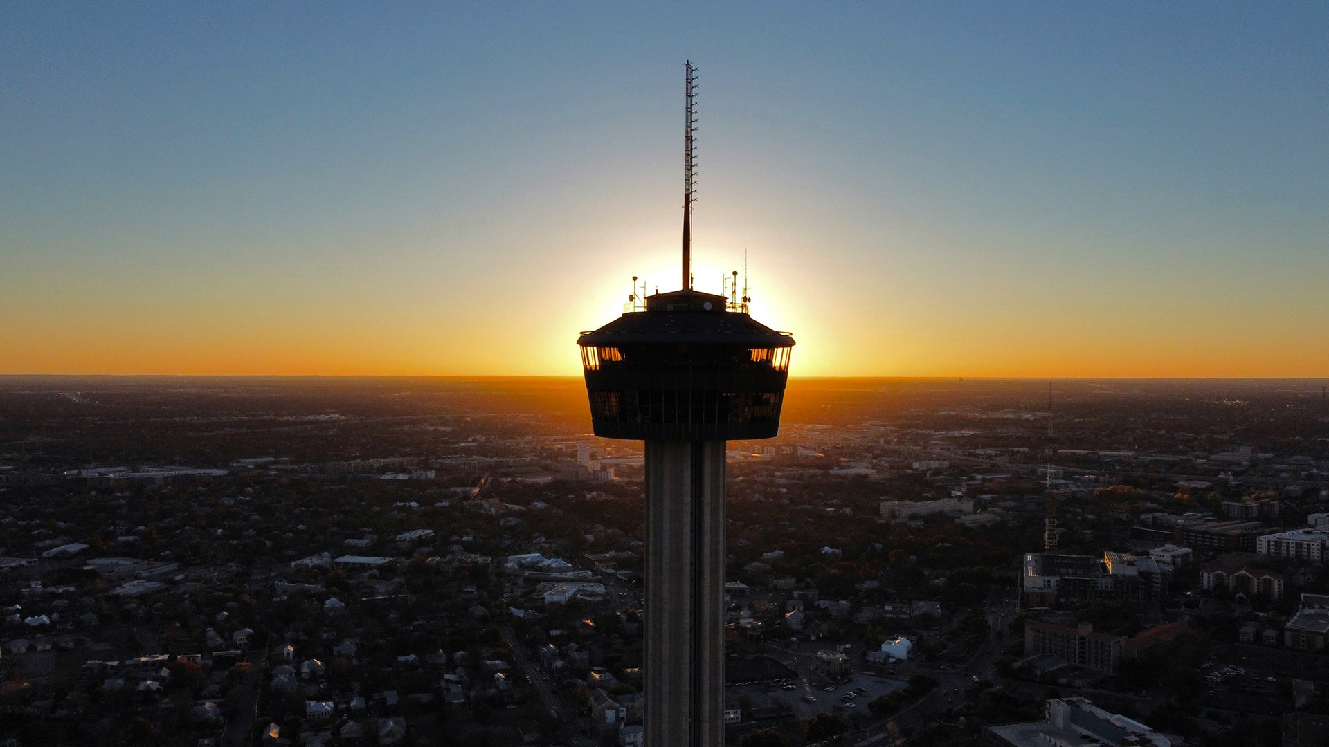 a tall tower set against the sunset with a view of the city below