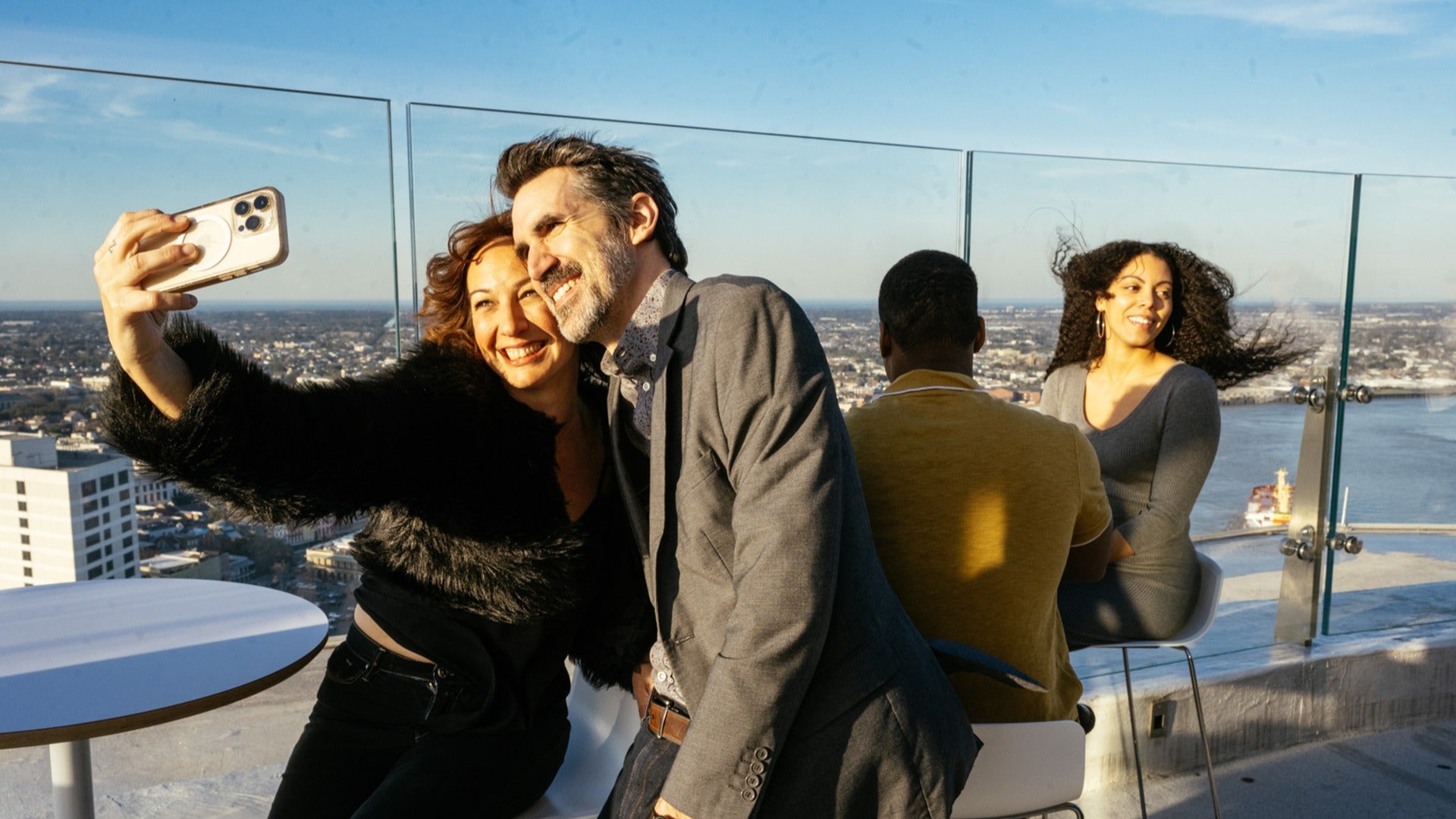 a couple of people taking selfies on a rooftop deck with a view of the city below