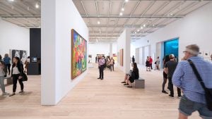 a group of people looking at various art exhibits with paintings on the walls