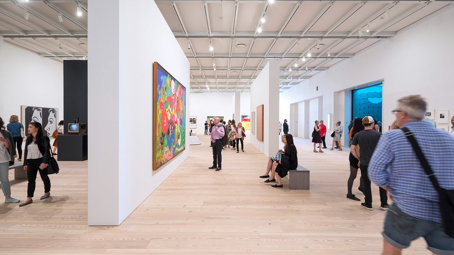 a group of people looking at various art exhibits with paintings on the walls