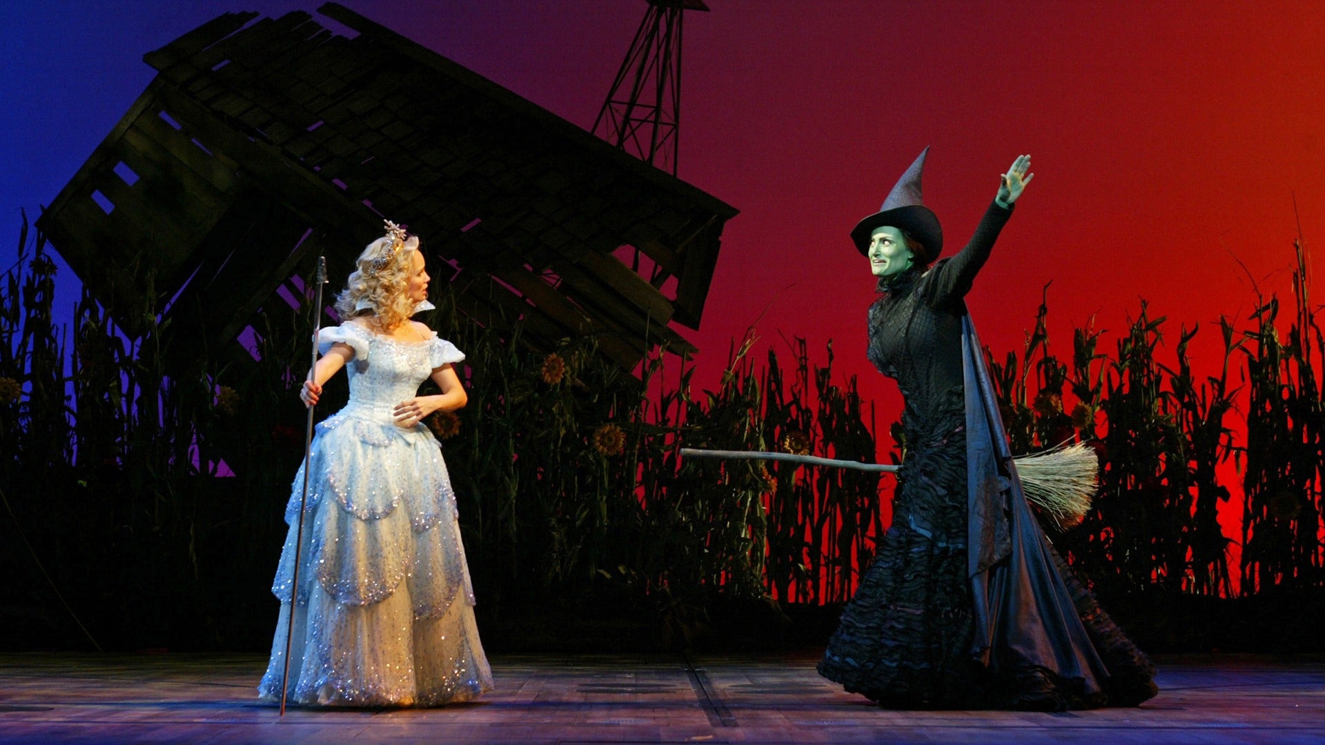 two actors in costumes on stage holding wands and brooms