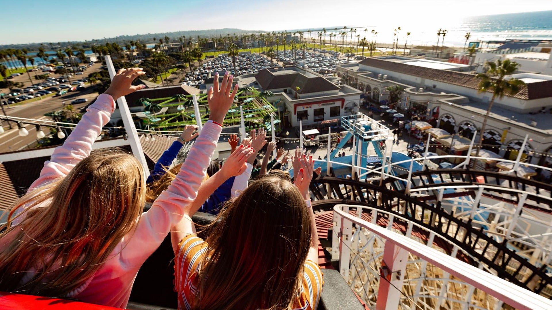 girls in a roller coaster raising their hands with a view of the bay below them