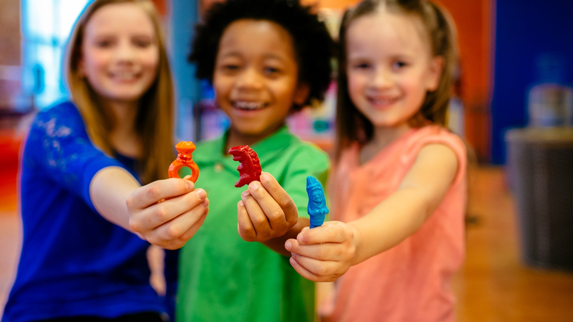 a group of kids happily holding up random shaped crayons