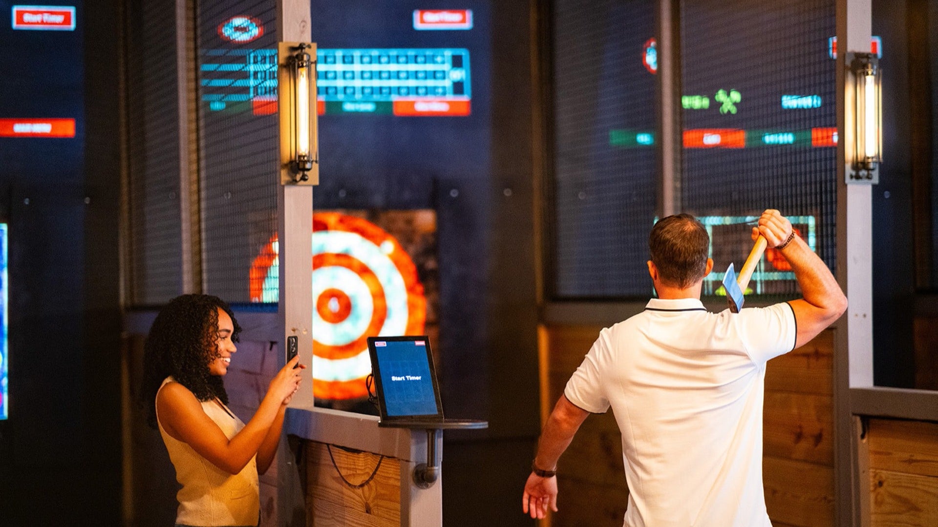 a woman taking a video of a man throwing an axe at an arcade