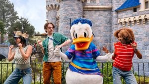 donald duck mascot dancing with three friends with the castle behind them