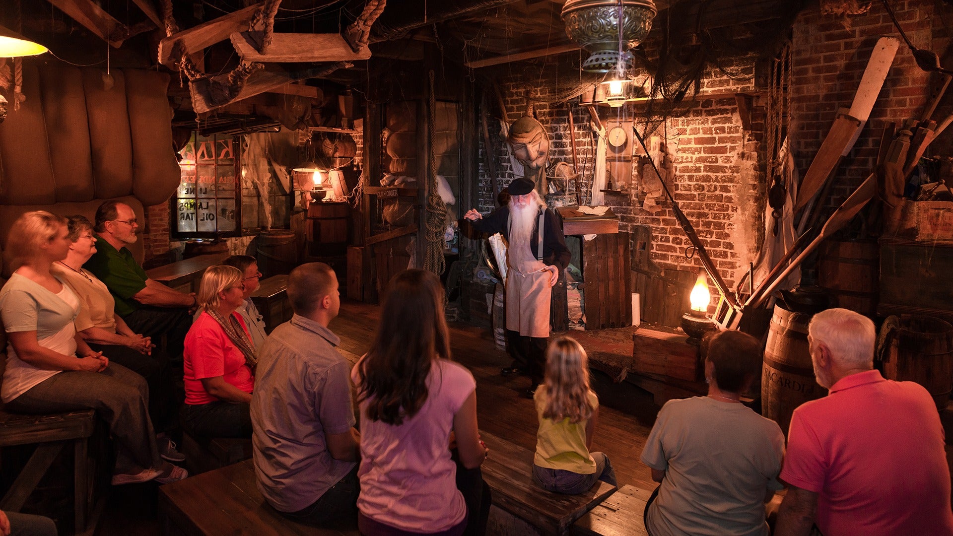 a group of people listening to a man in costume inside a haunted tavern