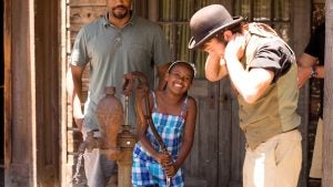 a child pumping water with men watching her