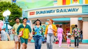 a group of friends eating churros and walking at a theme park with rides and attractions behind them