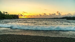view of the ocean from a black sand beach with the sunset behind