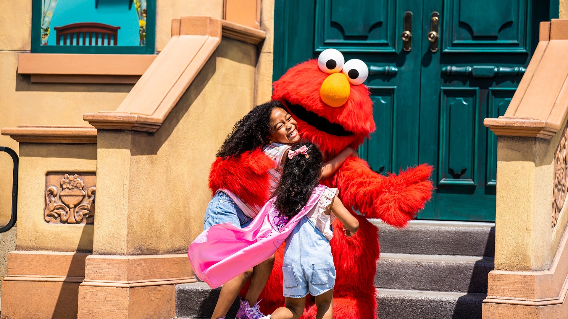 elmo hugging kids on the stairs leading up to a door