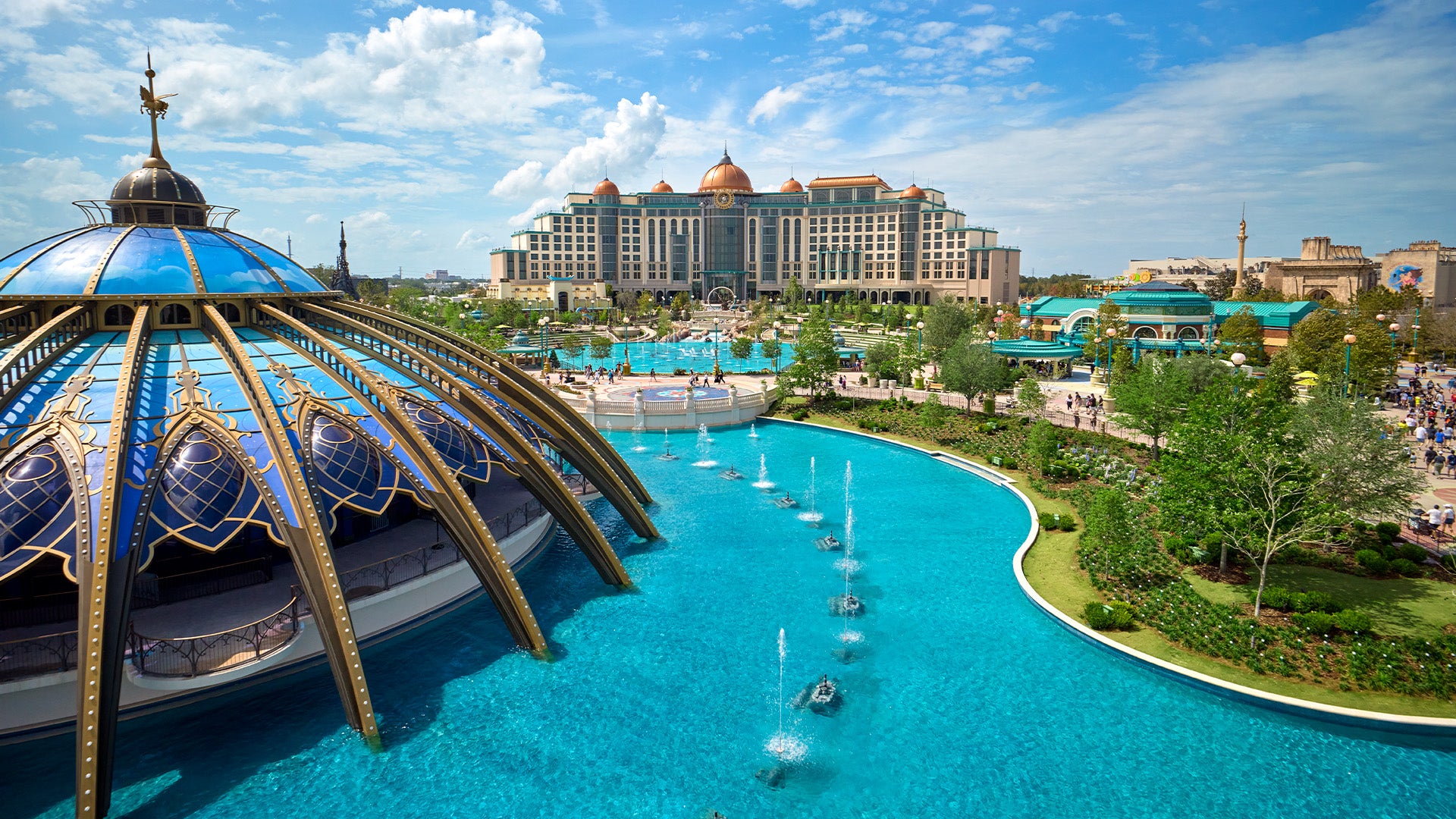 an overview of a theme park with water fountains and trees, and a hotel at the back