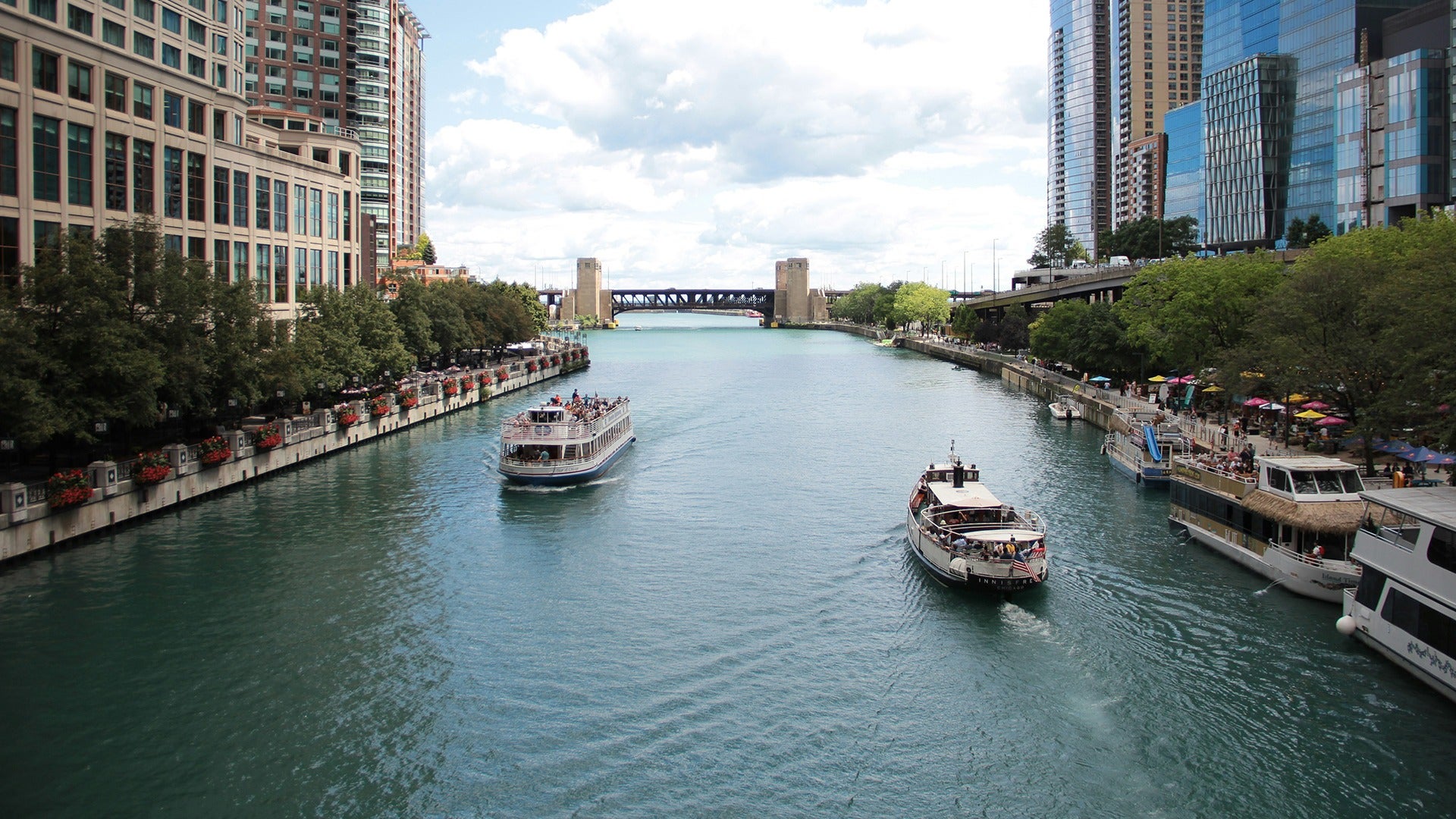 tour boats passing down a river in downtown chicago surrounded by buildings
