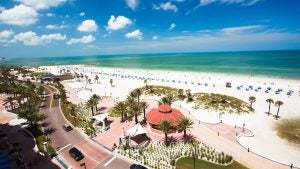 a beach lined with trees, beach chairs, people wandering and a roadside street