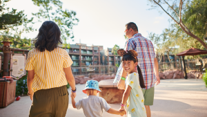 a family walking hand in hand towards a hotel, with a little girl smilling at the camera