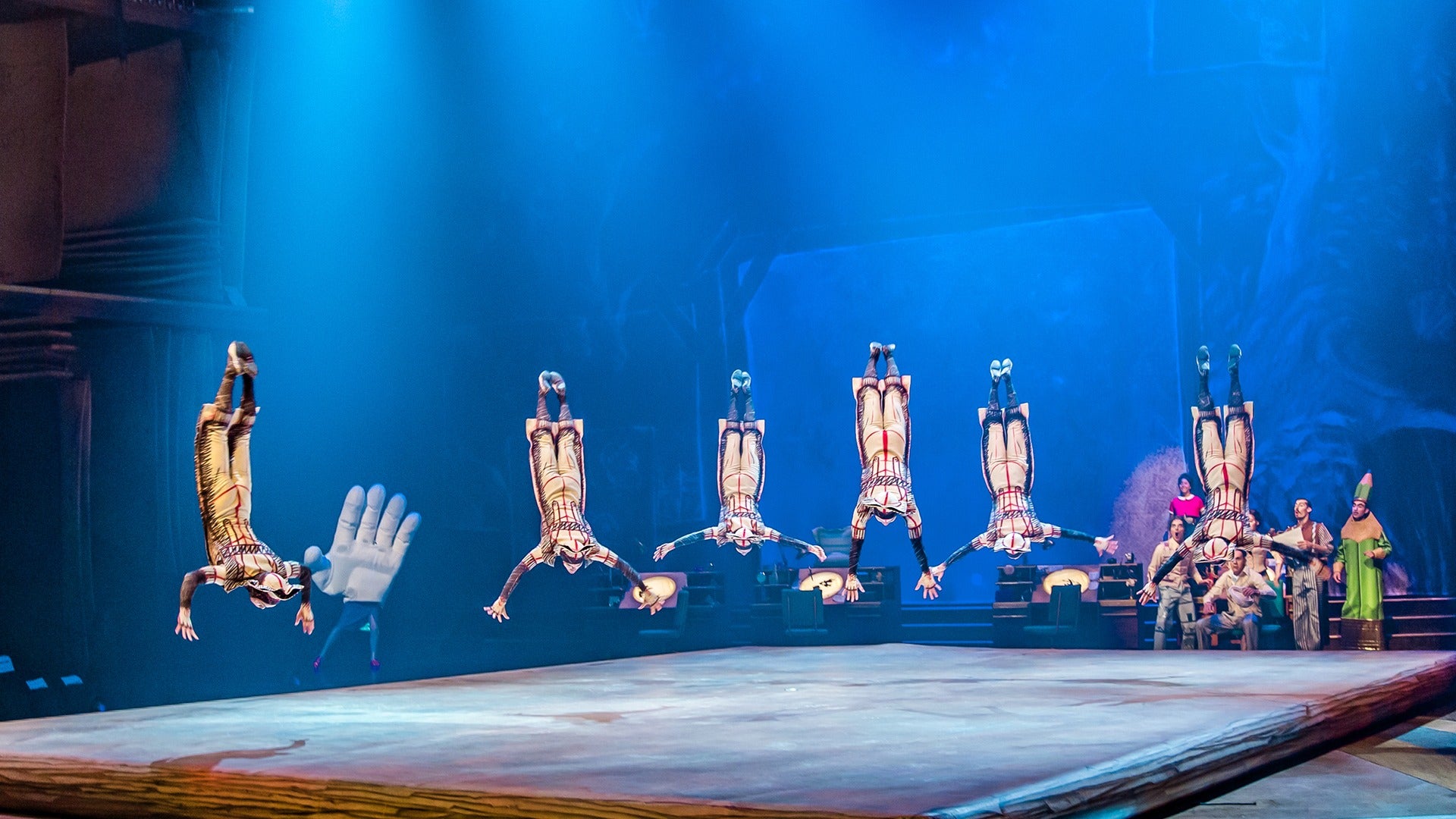 a bunch of acrobats performing upside down on stage with people watching at the back