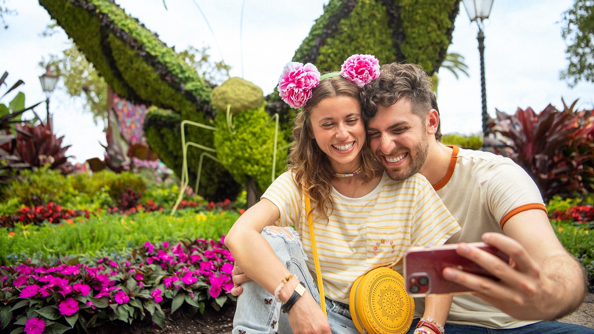 a couple taking a selfie in front of a garden with flowers and a butterfly shaped feature