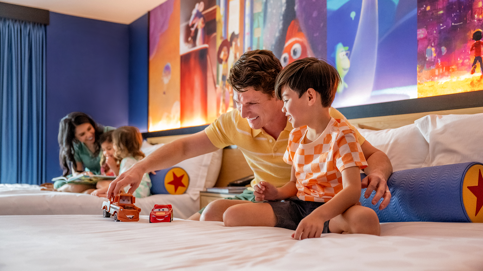 a father and son playing with toy trucks with his siblings on the other bed in a hotel