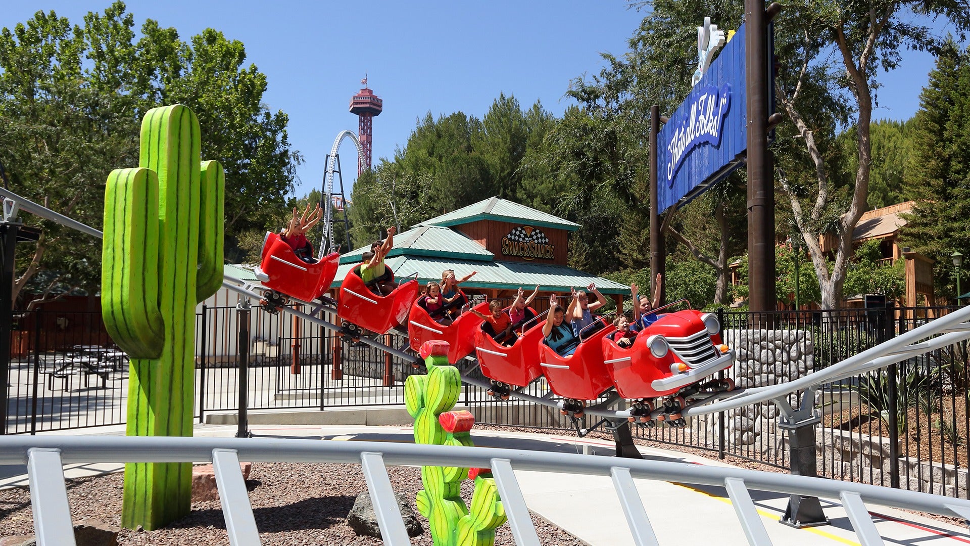 people in a small trolley roller coaster with trees at the back