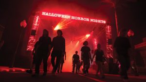 Crowds walking through the Halloween Horror Nights entrance gate surrounded by red fog and dramatic lighting