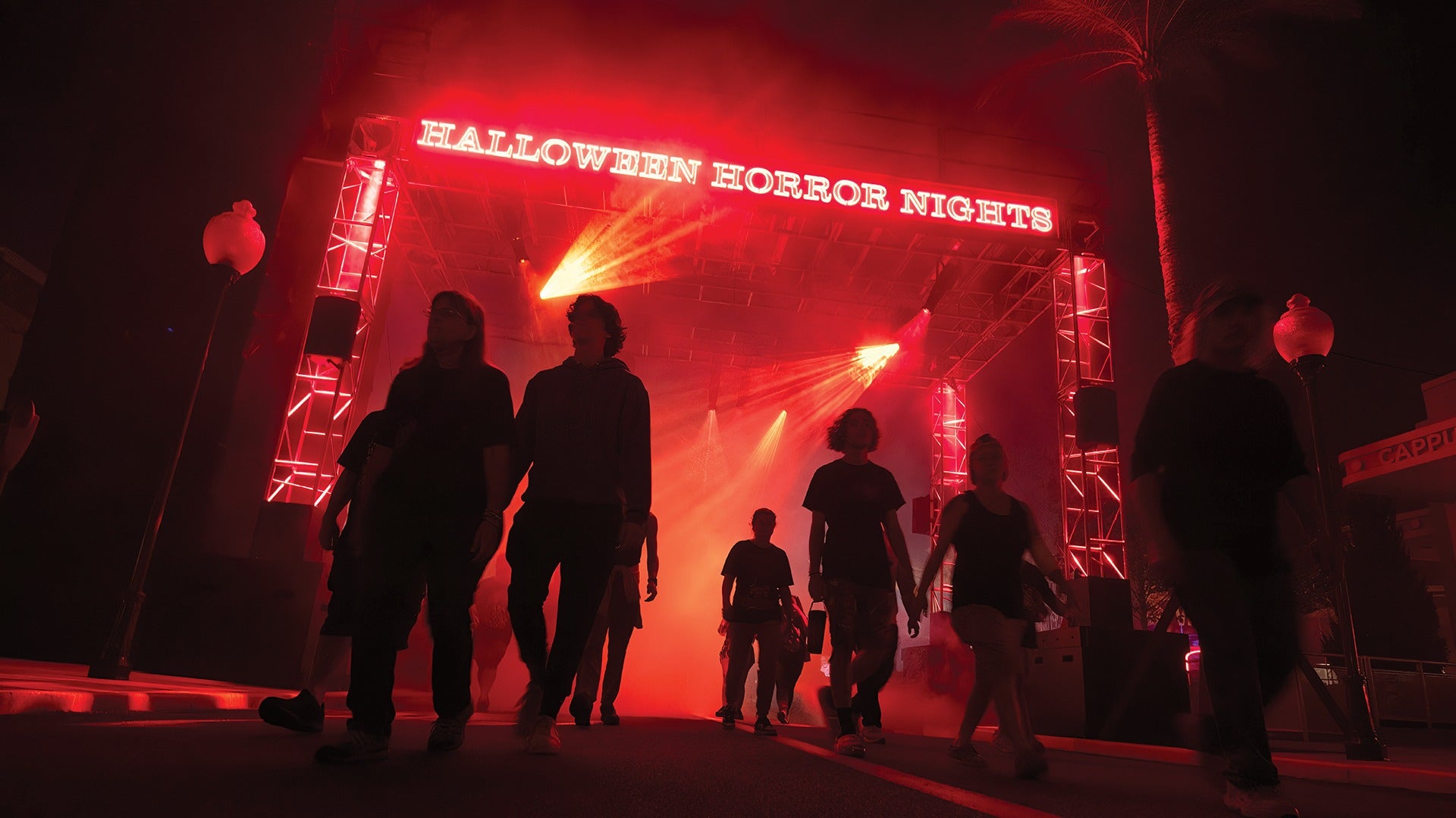 Crowds walking through the Halloween Horror Nights entrance gate surrounded by red fog and dramatic lighting