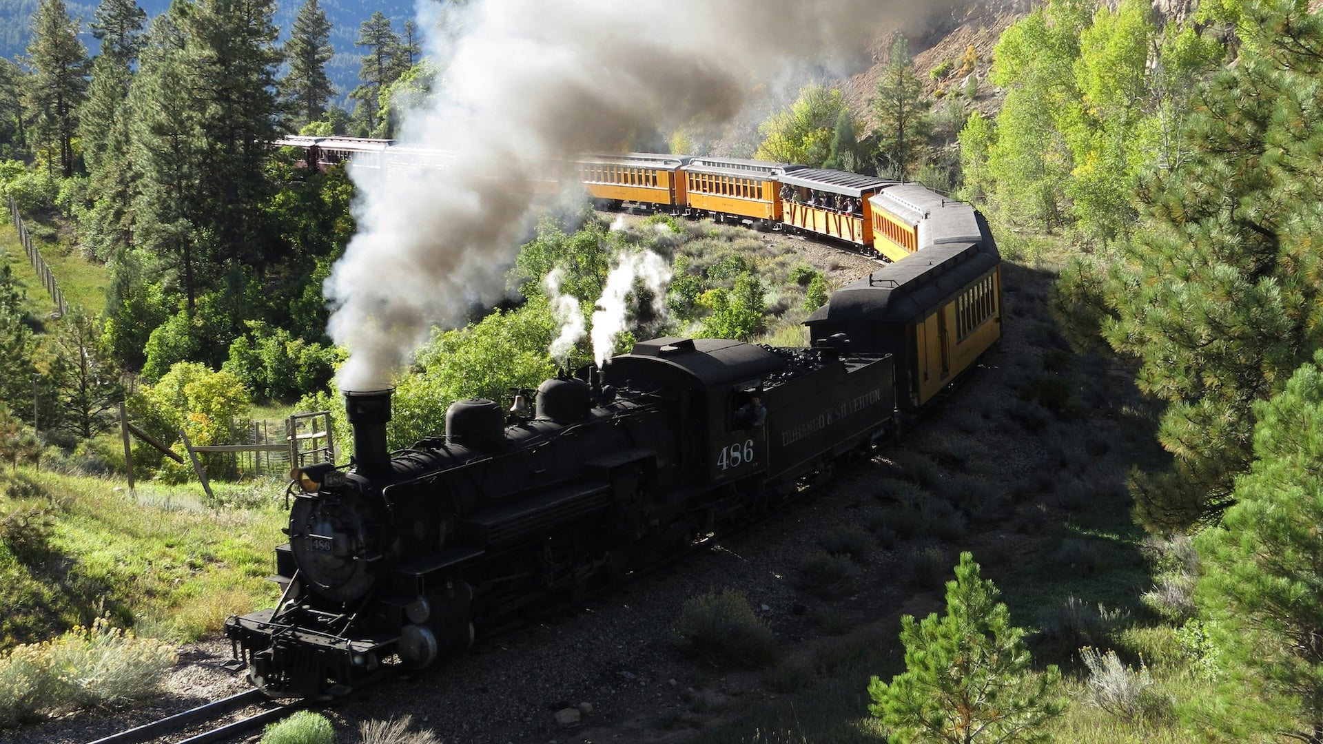 Black train with steam coming out of the stack in the mountains