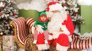 child dressed up as an elf sitting on Santa Claus' lap in room with green walls filled with Christmas decorations in Philadelphia Zoo, Philadelphia, Pennsylvania, USA