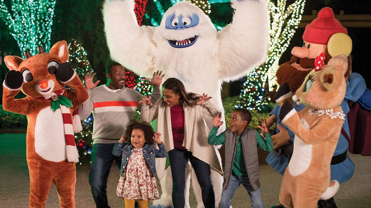 family posing for photo with mascots with trees covered in christmas lights in background at Christmas Town at Busch Gardens in Tampa Bay, Florida, USA