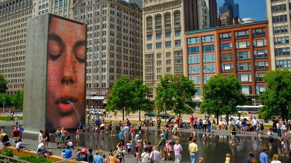 a crowd of people around the interactive installation called the Crown Fountain located in Millenium Park with trees and buildings in background in Millenium Park, Illinois, Chicago, USA