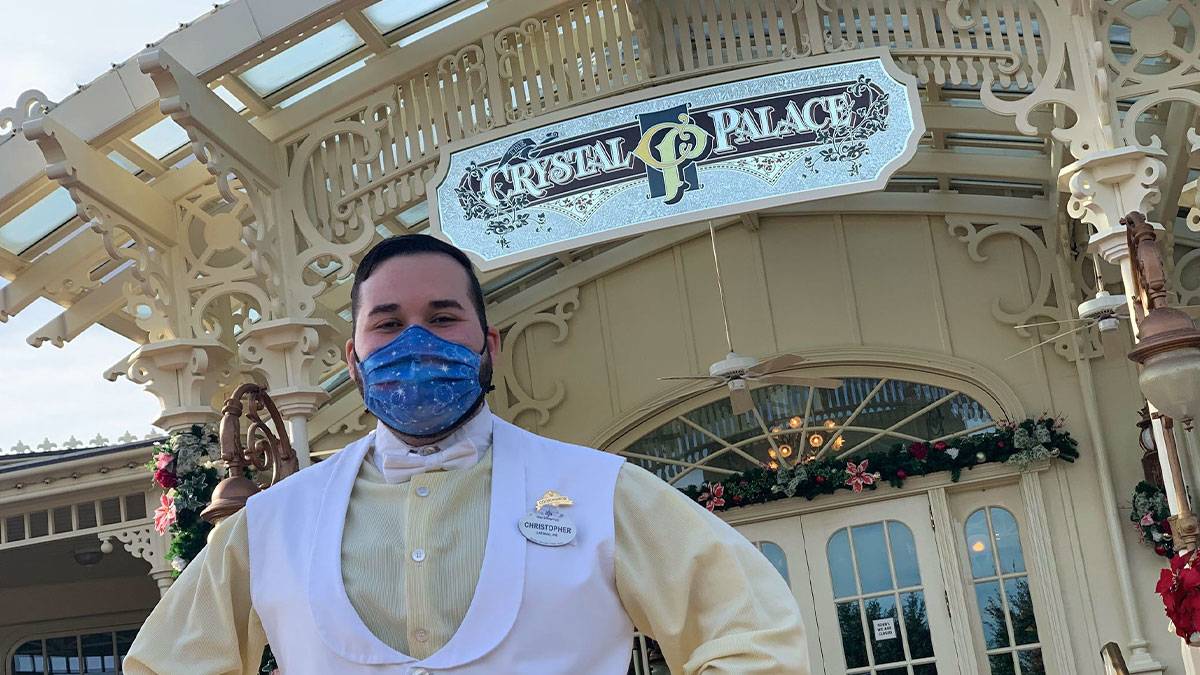 waiter wearing face mask at The Crystal Palace with exterior of establishment with sign in the background at Disneyworld in Orlando, Florida, USA