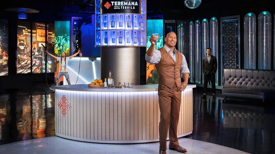 wax figure of Dwayne "The Rock" Johnson in holding glass in front of bar with other wax figures in the background at Madame Tussauds in Las Vegas, Nevada, USA
