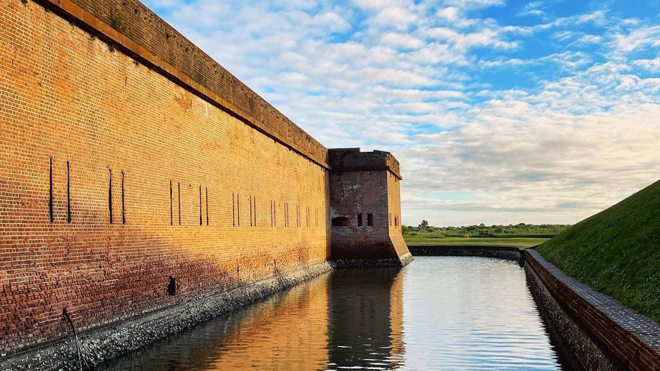 angled photo of Fort Pulaski wall with field in distance during daytime with blue sky and clouds in Savannah, Georgia, USA