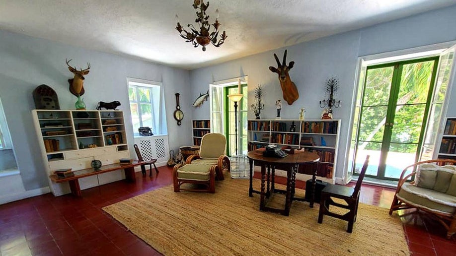 writing room of writer Ernest Hemingway with white walls decorated with animal head mounts and a chandelier and bookshelves also featuring the writer's typewriter on a table in Hemingway House, Key West, Florida, USA