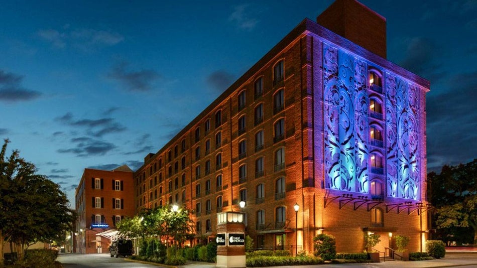 exterior of Hotel Indigo lit with colorful lighting surrounded by some trees during night in Savannah, Georgia, USA