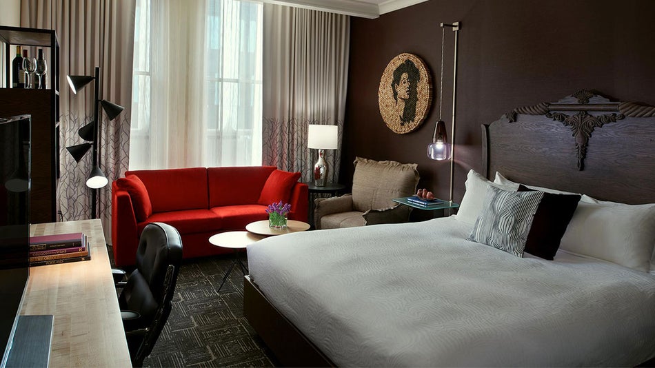 room with dark brown walls, red sofa, and bed with intricate carved headboard and tv set in Kimpton Hotel Vintage, Portland, Oregon, USA