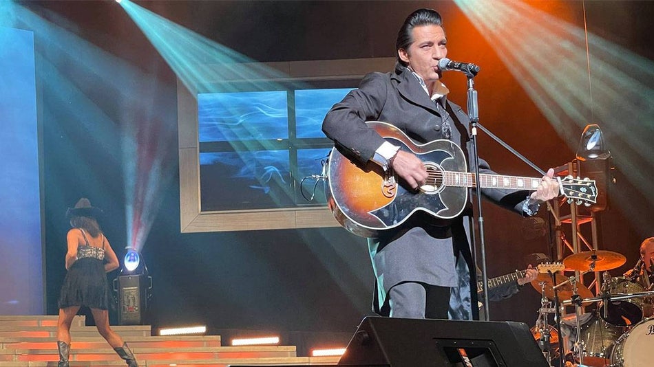 Johnny Cash impersonator performing with guitar on stage with backup dancers and drummer at Legends of Country in Branson, Missouri, USA