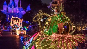 Disney Character actor in Tinkerbell costume riding float covered in lights with other floats and dineyland castle in background at Mainstreet Electrical Parade in Anaheim, California, USA