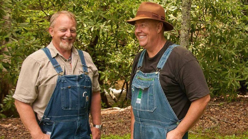 Mark Ramsey and Digger Manes from Discovery Moonshine TV in overalls smiling for a photograph with plants in the background in Tennessee, USA