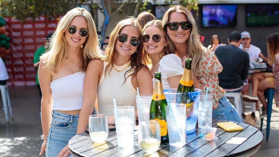 friends wearing shades with glasses and champagne bottles at outdoor area at Mavericks Beach Club during day in San Diego, California, USA