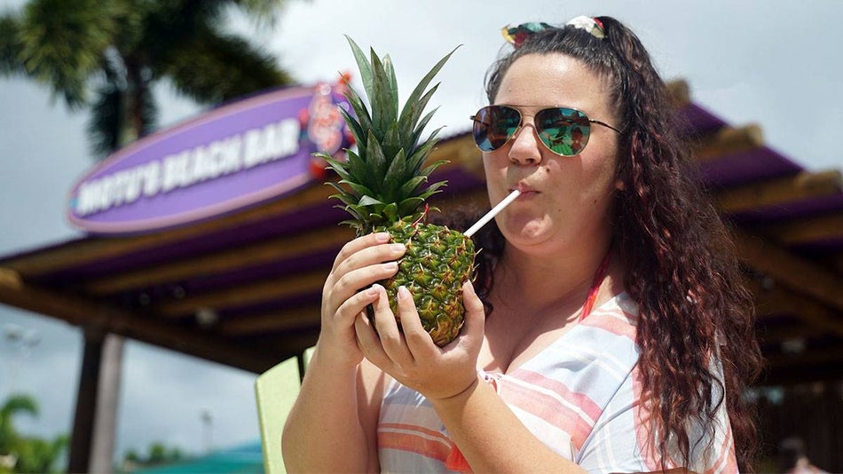 woman in sunglasses enjoying drink incased in fresh pineapple at Motus Beach Bar Aquatica in Orlando, Florida, USA