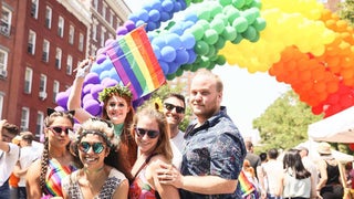 group of friends posing for photo under balloon arch with crowd in background at NYC Pride Festival, New York City, New York, USA