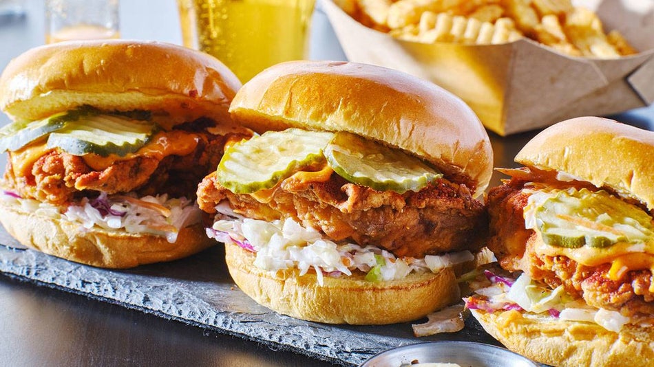 a row of three Nashville Hot Chicken Sandwiches with drinks and fries in the background