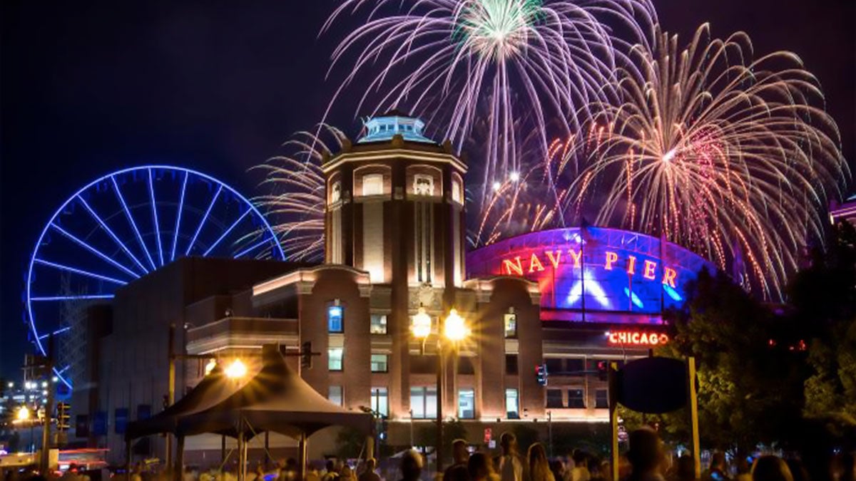 building and lit up Navy Pier sign with fireworks in the background at night at Navy Pier during summer in Chicago, Illinois, USA