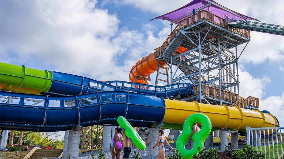 group of friends in swimsuits carrying green floaties walking towards pool slides at Rapids Racer and Wahoo Remix Adventure Island in Tampa, Florida, USA