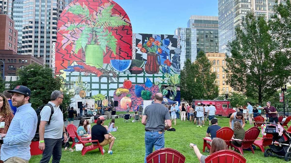 people spending day at Rose Kennedy Greenway some seated on red chairs with colorful mural, food truck, and buildings in background in Boston, Massachusettes, USA